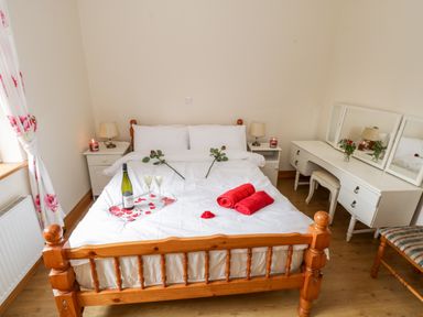 A bedroom with a wooden bed white bedding red roses and towels a white dressing table with mirrors at Lough Mask Road Fishing Cottage in Ballinrobe County Mayo