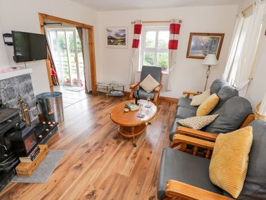 A living room with wooden floor a grey leather sofa and armchair a wooden coffee table and a fireplace at Lough Mask Road Fishing Cottage in Ballinrobe County Mayo