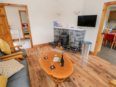 A living room with wooden floor a fireplace and a coffee table with drinks and a book at Lough Mask Road Fishing Cottage in Ballinrobe County Mayo