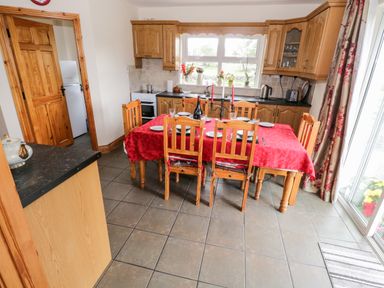 A kitchen with wooden cabinets a dining table covered with red cloth wooden chairs and windows with floral curtains at Lough Mask Road Fishing Cottage Ballinrobe County Mayo