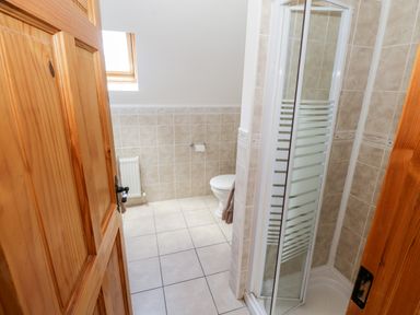 A bathroom with a tiled shower enclosure wooden doors a toilet a radiator and a skylight window at Lough Mask Road Fishing Cottage Ballinrobe County Mayo
