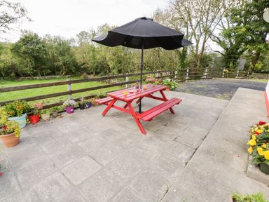 An outdoor patio with a red picnic table and black umbrella surrounded by potted plants at Lough Mask Road Fishing Cottage in Ballinrobe County Mayo