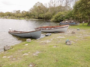 Several wooden boats tied to concrete blocks on the shore of a lake with trees in the background at Lough Mask Road Fishing Cottage in Ballinrobe County Mayo