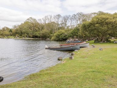A lakeside scene with rowboats moored on the shore and trees in the background at Lough Mask Road Fishing Cottage in Ballinrobe County Mayo