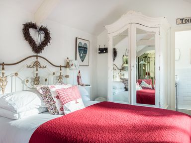 A bedroom with a metal bed frame red bedding pillows a white wardrobe with mirrors and a wreath on the wall at The Snug in Rescorla near St Austell