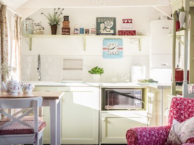 A kitchen with a microwave in a cabinet and a red chair at The Snug in Rescorla near St Austell