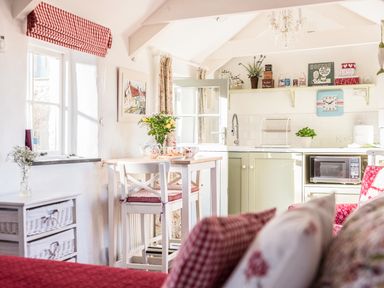 A kitchen and dining area with a table, chairs, shelves with kitchen items, and a microwave at The Snug in Rescorla near St Austell