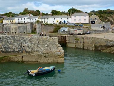 A small boat floating in a harbor with stone walls and houses in the background at The Snug in Rescorla near St Austell
