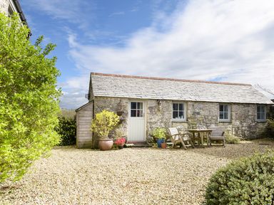 A stone cottage with three windows wooden door and outdoor table with chairs surrounded by plants at The Snug in Rescorla near St Austell