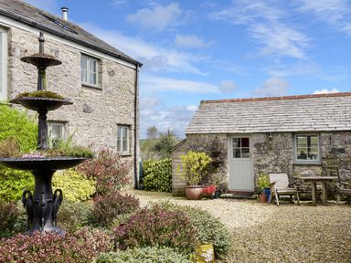 An exterior courtyard with stone buildings plants and a metal fountain at The Snug in Rescorla near St Austell