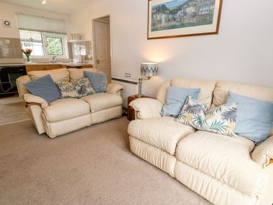 A living room with two cream sofas with cushions a lamp on a side table and a kitchen area with a window and sink at Brook Haven Rosecraddoc Lodge near Liskeard Cornwall