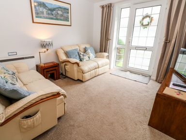 A living room with two beige sofas a wooden side table a lamp a painting on the wall and a door with windows at Brook Haven Rosecraddoc Lodge near Liskeard Cornwall