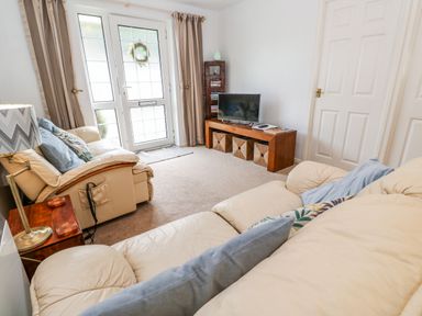 A living room with two cream sofas a wooden TV stand with baskets and a lamp on a side table at Brook Haven Rosecraddoc Lodge near Liskeard Cornwall