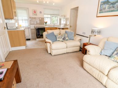 A living room with cream sofas and blue cushions next to a small kitchen with wooden cabinets at Brook Haven Rosecraddoc Lodge near Liskeard Cornwall