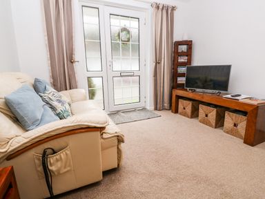 A living room with a beige leather sofa with cushions and a wooden TV stand with a television and storage baskets at Brook Haven in Rosecraddoc Lodge near Liskeard Cornwall
