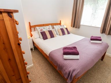 A bedroom with a double bed covered with a purple blanket and pillows near a window at Brook Haven Rosecraddoc Lodge near Liskeard Cornwall