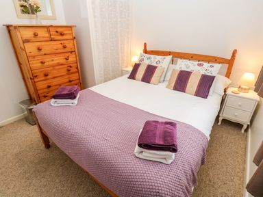 A bedroom with a wooden double bed covered in white and purple bedding a wooden chest of drawers and a bedside cabinet with a lamp at Brook Haven in Rosecraddoc Lodge near Liskeard Cornwall