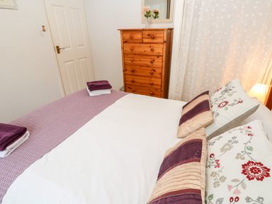 A bedroom with a bed with white and purple linens a wooden chest of drawers and a door at Brook Haven Rosecraddoc Lodge near Liskeard Cornwall