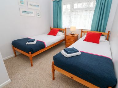 A bedroom with two single beds with blue blankets and red pillows a wooden nightstand with a lamp and pictures on the wall at Brook Haven Rosecraddoc Lodge near Liskeard Cornwall