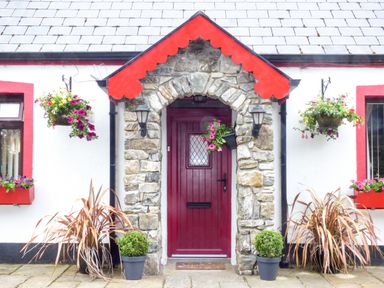 The front entrance of a cottage with a red door stone arch and hanging flower baskets at Cookies Cottage in Ballyshannon County Donegal