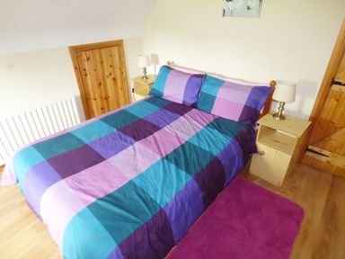A bedroom with a bed with a multicolored checkered duvet two wooden nightstands with lamps and a purple rug on the floor at Cookies Cottage Ballyshannon County Donegal