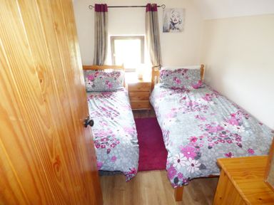 A small bedroom with two single beds with floral bedding and a wooden nightstand between them at Cookies Cottage Ballyshannon County Donegal