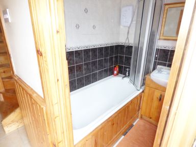 A bathroom with a bathtub a shower unit a sink with a cabinet and wooden paneling at Cookies Cottage in Ballyshannon County Donegal