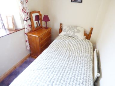 A bedroom with a single bed a wooden dresser with a mirror and a lamp by a window at Cookies Cottage in Ballyshannon County Donegal