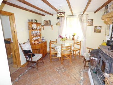 A dining area with a round table and chairs a wooden cabinet with crockery a window with curtains and a wood burning stove at Cookies Cottage in Ballyshannon County Donegal