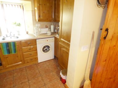 A kitchen with wooden cabinets a washing machine a sink a kettle and a broom at Cookies Cottage in Ballyshannon County Donegal