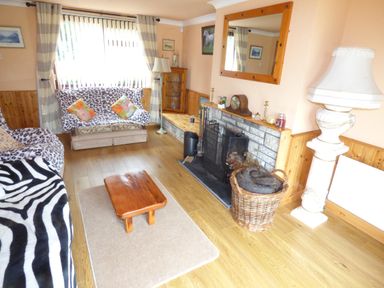 A living room with sofas covered in animal print throws a wooden coffee table a fireplace with a basket of logs and a large mirror above it at Cookies Cottage Ballyshannon County Donegal