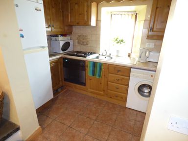 A kitchen with wooden cabinets white appliances a washing machine a refrigerator a microwave an oven a kettle and a window at Cookies Cottage Ballyshannon County Donegal