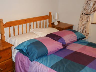 A bedroom with a wooden bed frame a multicolored bedspread two wooden nightstands a lamp and a floral curtain at Cookies Cottage in Ballyshannon County Donegal