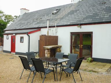 An outdoor patio area with a table and six chairs outside a white cottage with a slate roof at Cookies Cottage in Ballyshannon County Donegal