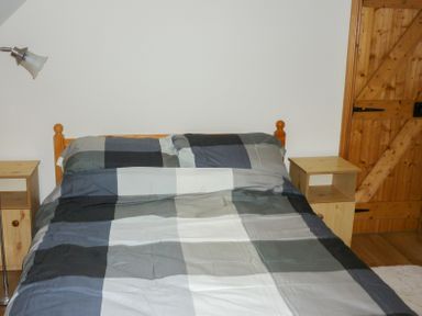 A bedroom with a double bed plaid bedding two wooden bedside tables a wooden door and a floor lamp at Cookies Cottage in Ballyshannon County Donegal