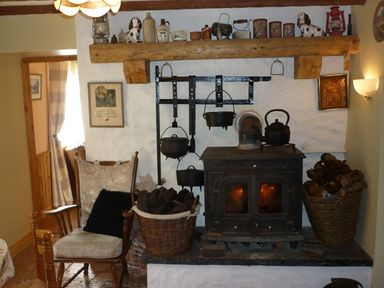 A room with a wood burning stove a rocking chair baskets of firewood and hanging pots at Cookies Cottage Ballyshannon County Donegal
