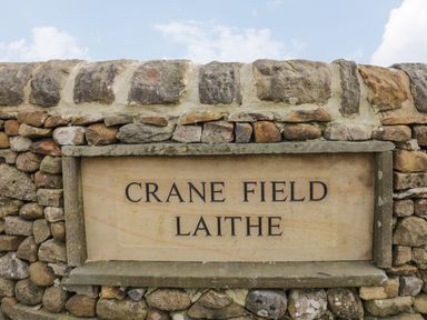 A stone wall with a sign reading Crane Field Laithe Otterburn North Yorkshire