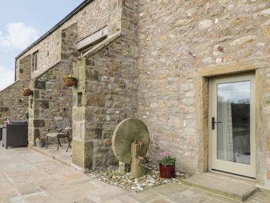 A stone patio with outdoor chairs pots of flowers and an old millstone at Crane Field Laithe in Otterburn North Yorkshire