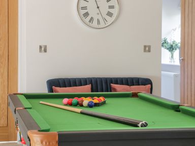 A pool table with pool balls and cue sticks in a room with a clock on the wall and a sofa with cushions at Crane Field Laithe in Otterburn North Yorkshire