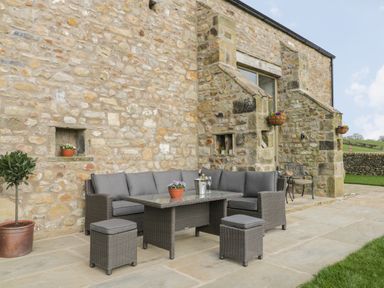 An outdoor seating area with a gray cushioned sofa set and table against a stone wall at Crane Field Laithe in Otterburn North Yorkshire