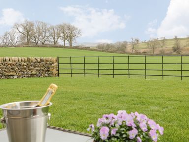 A grassy field with a stone wall and a metal gate with a bucket and flowers in the foreground at Crane Field Laithe in Otterburn North Yorkshire