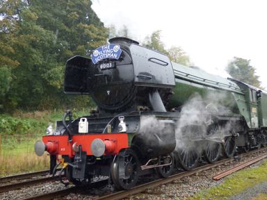 A steam locomotive train named The Flying Scotsman on railway tracks with trees nearby at Crane Field Laithe in Otterburn North Yorkshire