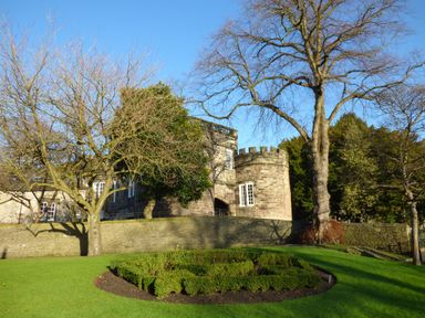 A garden with trimmed bushes and bare trees in front of a stone castle building Crane Field Laithe Otterburn North Yorkshire