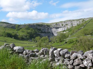 A grassy landscape with stone walls and cliffs under a blue sky at Crane Field Laithe in Otterburn North Yorkshire