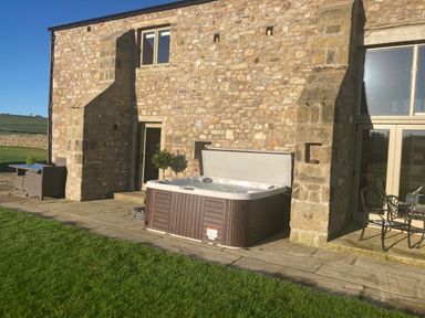 An outdoor patio area with a hot tub furniture and stone building exterior at Crane Field Laithe in Otterburn North Yorkshire