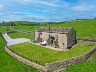 A stone farmhouse with a fenced lawn and patio with outdoor furniture and a hot tub in a rural area at Crane Field Laithe in Otterburn North Yorkshire