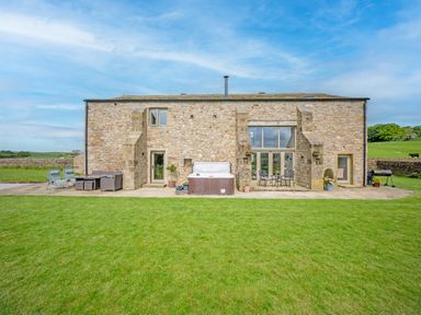 Stone barn with patio furniture and a hot tub on a lawn at Crane Field Laithe in Otterburn North Yorkshire