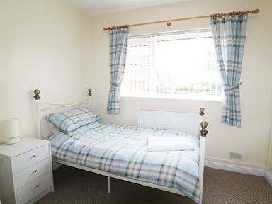A bedroom with a single bed with plaid bedding a white bedside table with a lamp and a window with plaid curtains at Anneddle in Four Mile Bridge