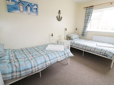 A bedroom with two single beds with plaid bedding and a window with plaid curtains at Anneddle in Four Mile Bridge