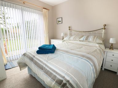 A bedroom with a bed with striped bedding and blue towels on it two bedside tables with lamps and a window with vertical blinds and curtains at Anneddle in Four Mile Bridge